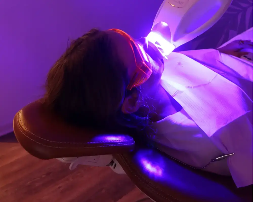 A patient's face lit by blue light during a clinical Zoom teeth whitening session.