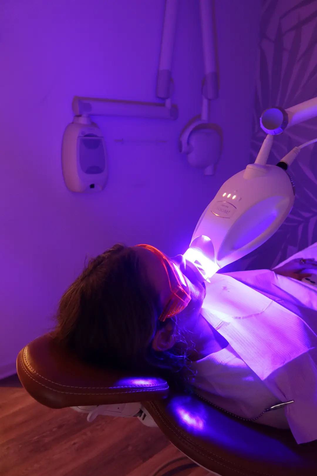 Patient relaxing under blue LED lamp for a professional teeth whitening treatment.